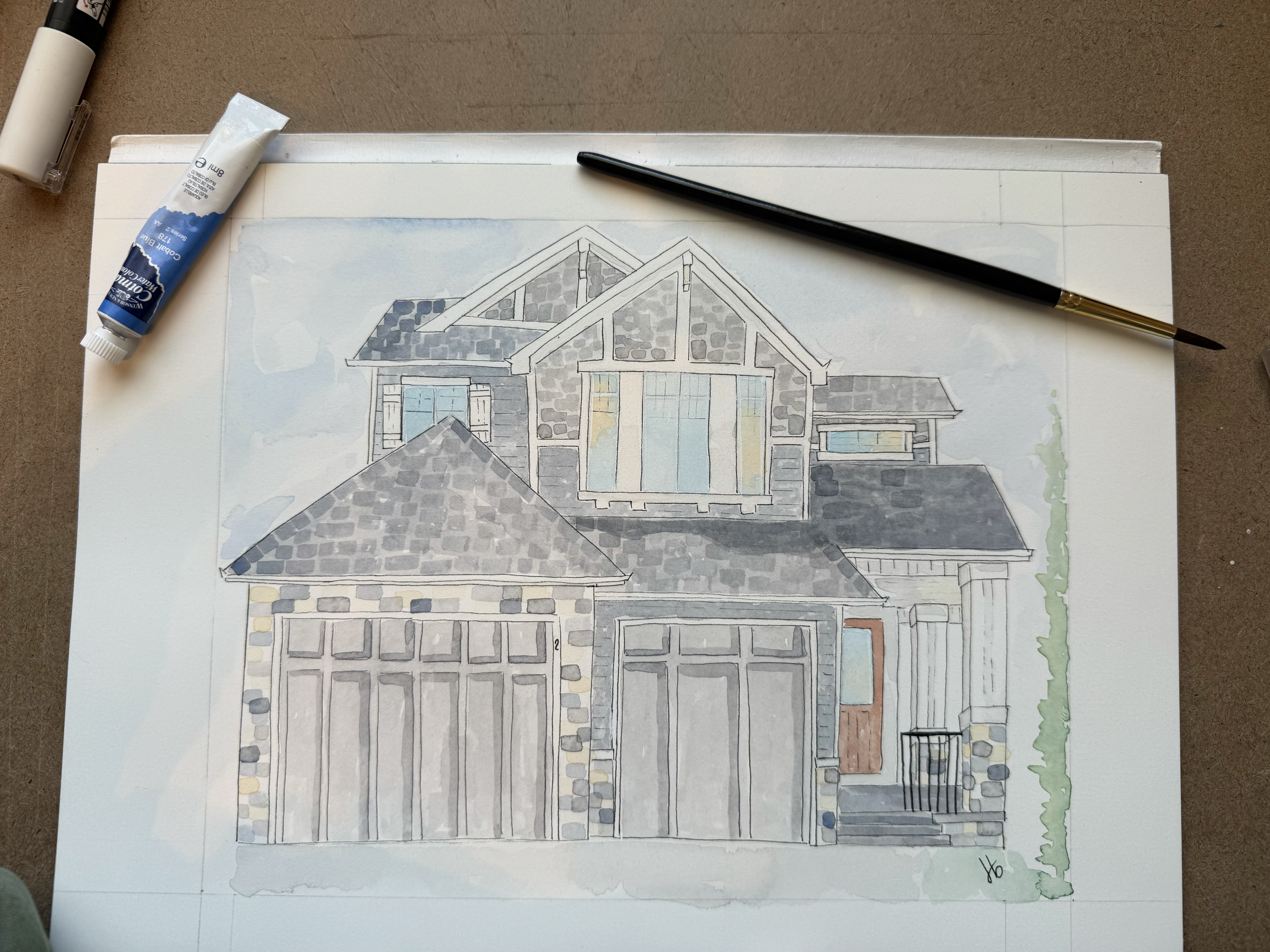 Watercolor of a home with paintbrush and pigment tube alongside
