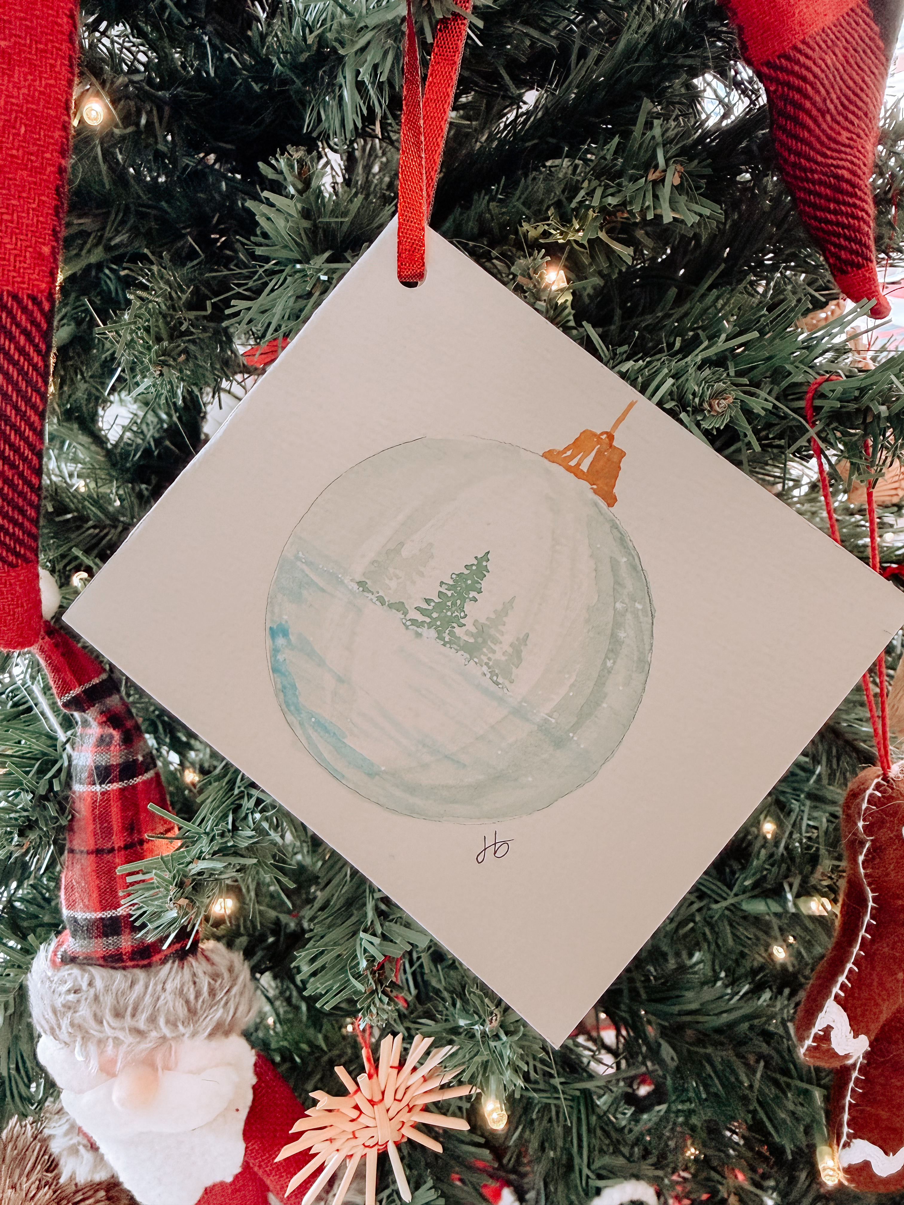 Watercolor ornament card depicting a snow-globe bauble with an evergreen inside, hung on a Christmas tree