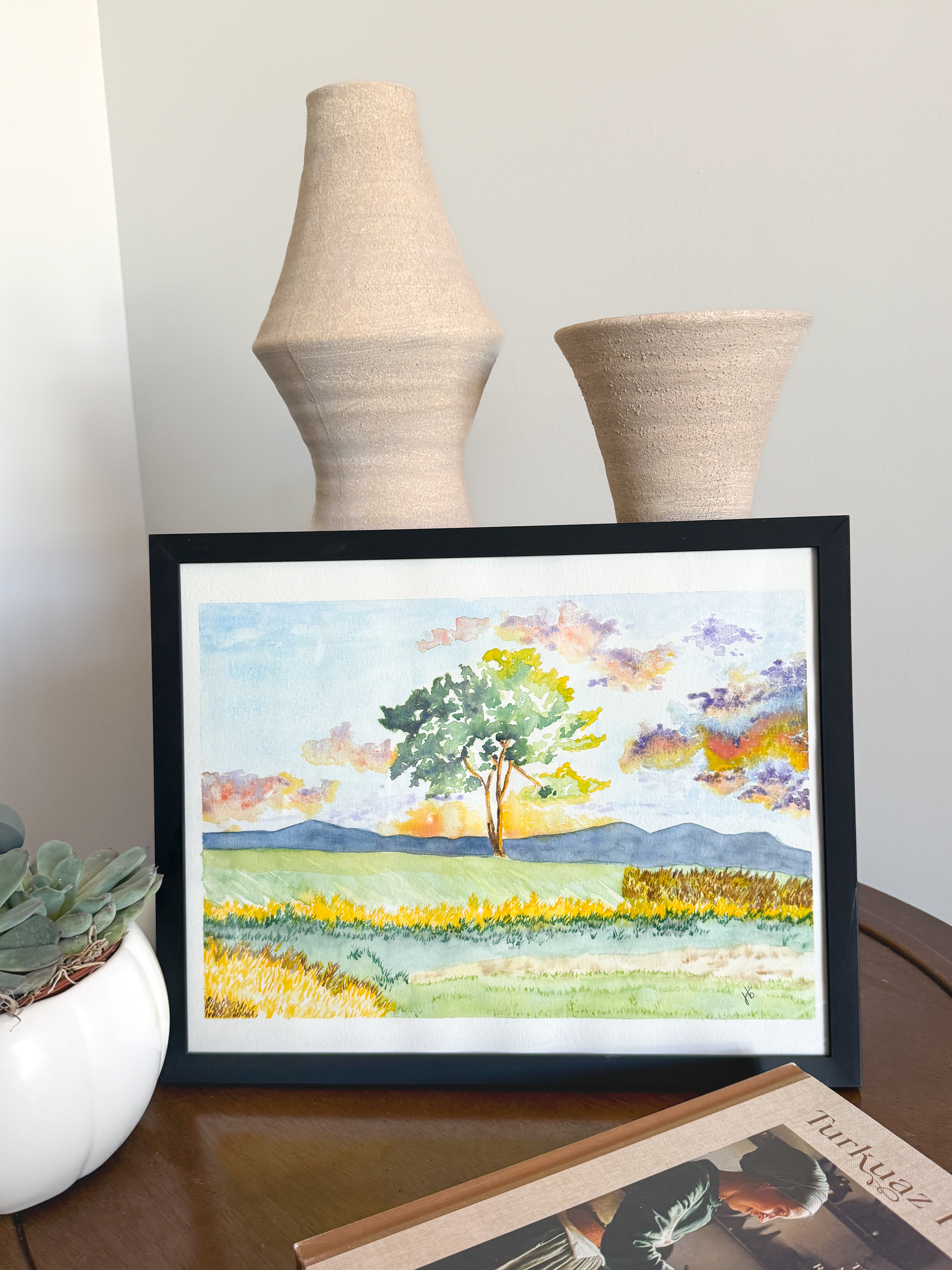 Framed watercolor of a single tree at the centre of a wide prairie under a sunset sky