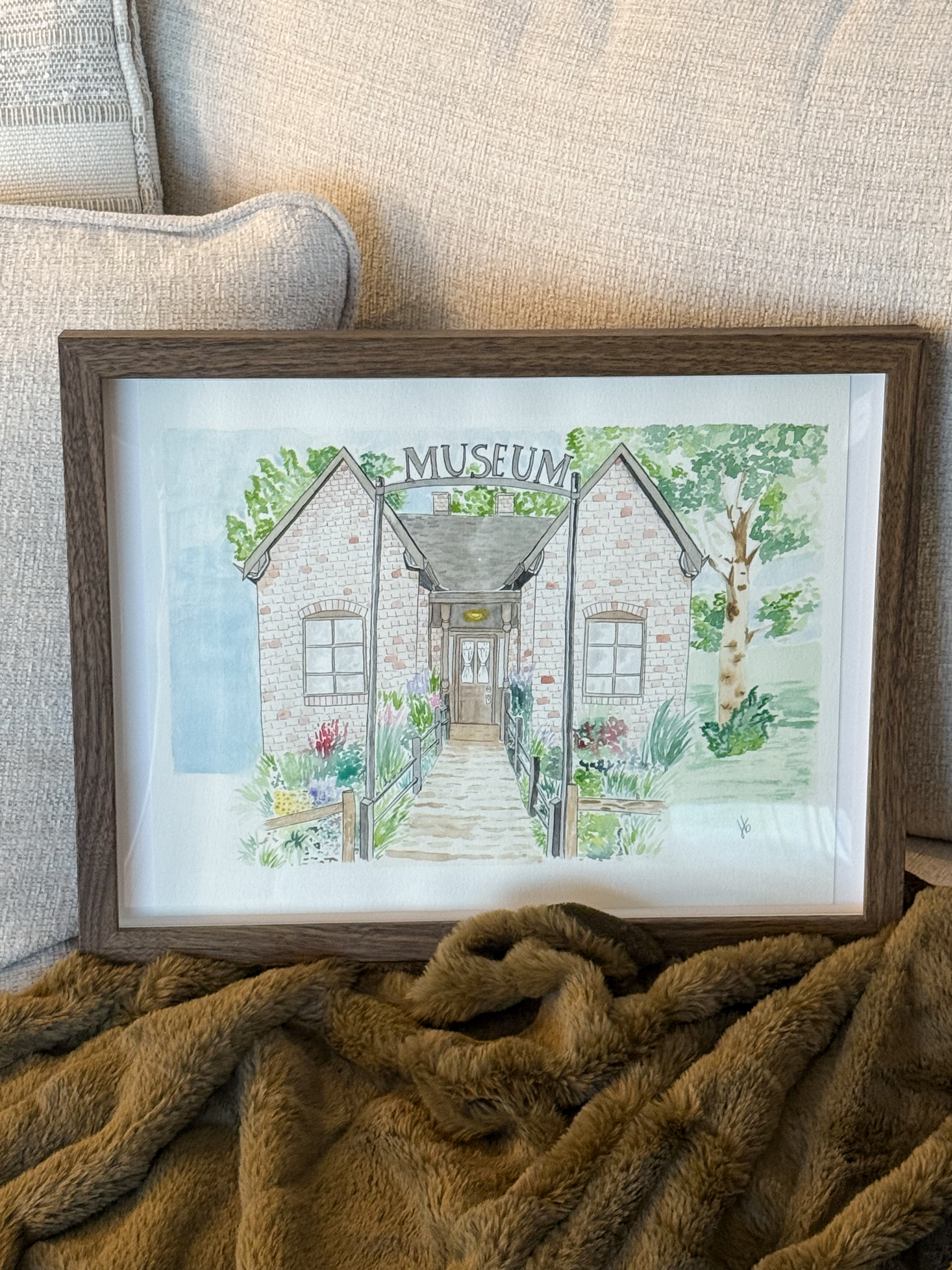 Framed watercolor of a small brick museum with garden beds along the path