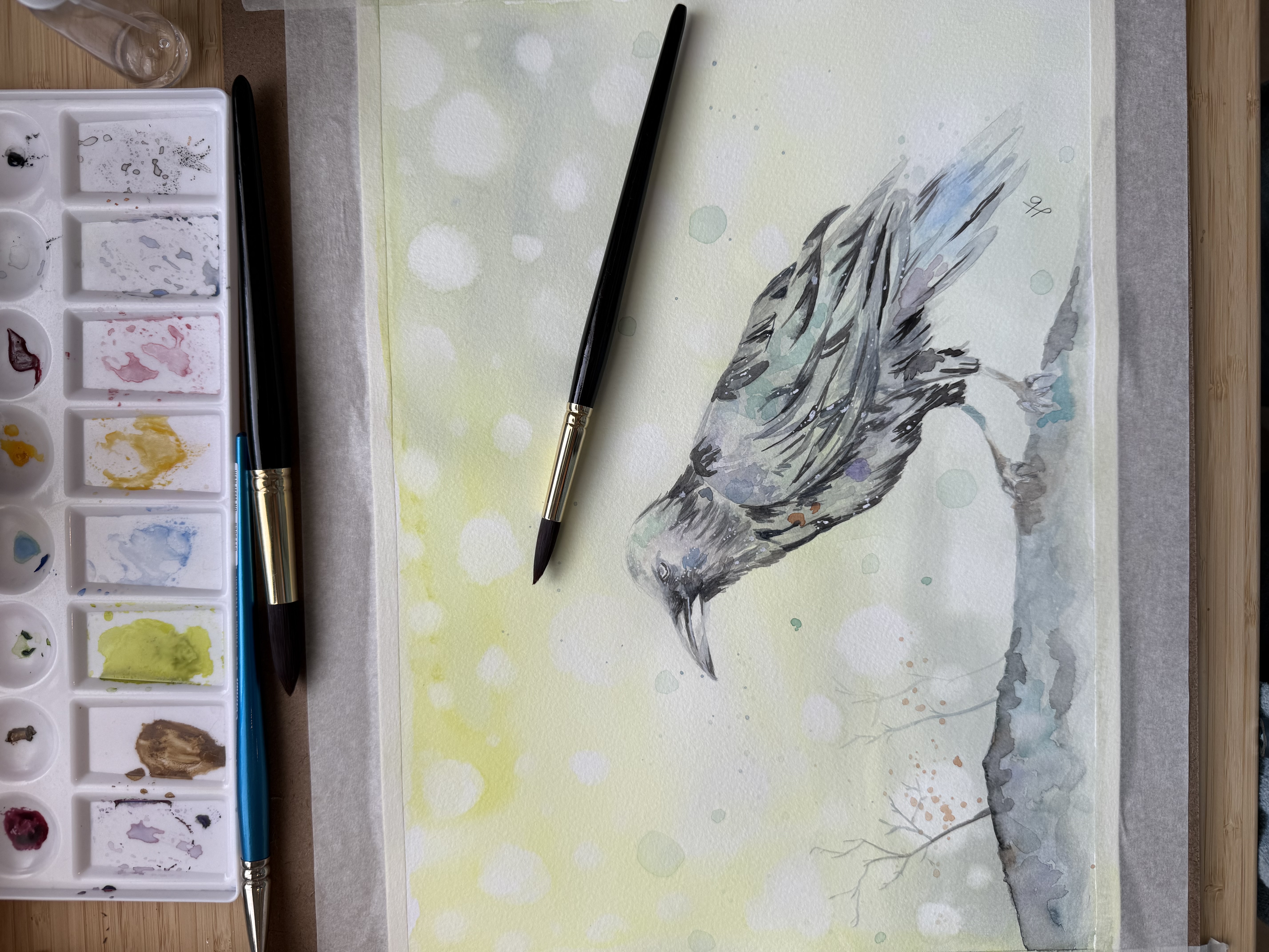 Watercolor of a crow with white speckled background, beside an artist's palette