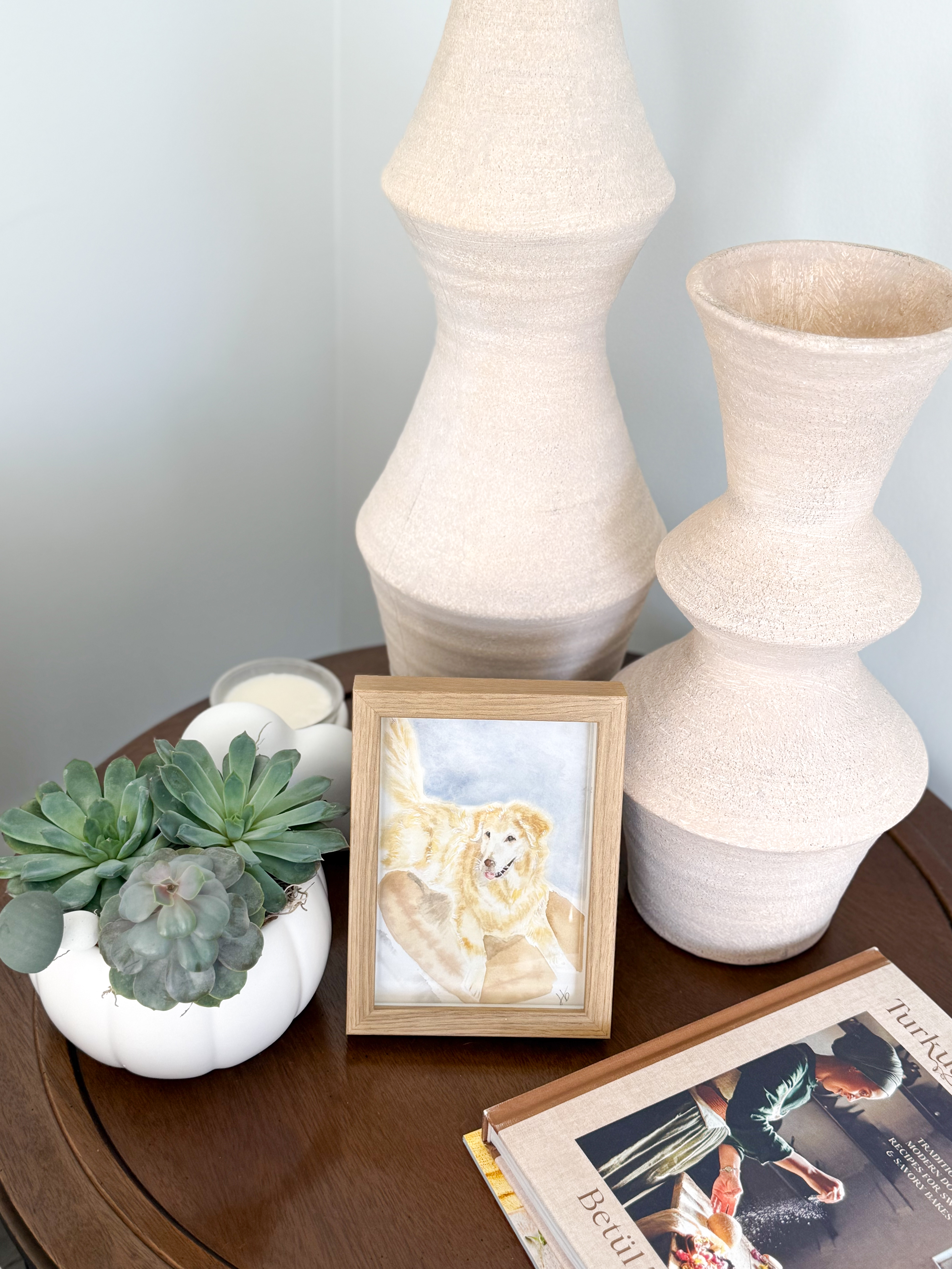 Framed watercolor portrait of a golden retriever displayed on a side table with vases and a succulent